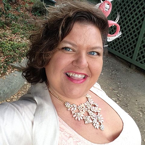 Person with pink lipstick and flower necklace smiling at the camear