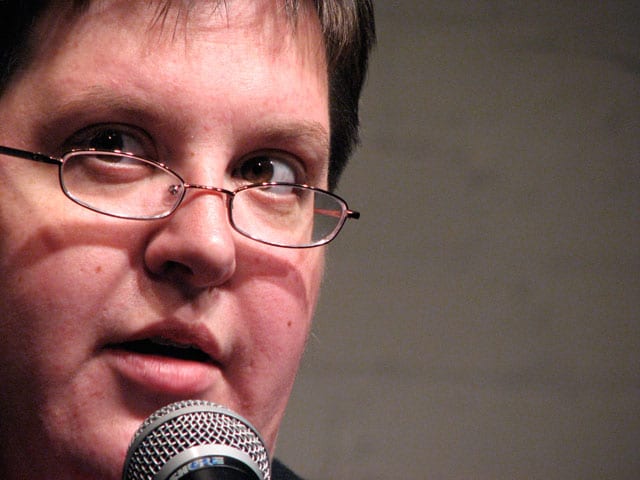 Image of a person wearing glasses speaking into a microphone