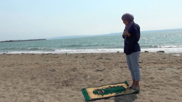 photo of woman stanging in front of prayer rug on a beach